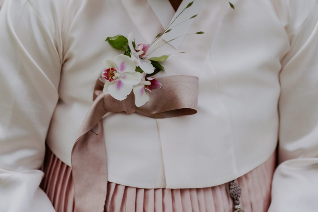 Close-up of a person wearing a traditional Korean hanbok with a pink ribbon and floral decoration on the chest area, perfect for a Korean wedding celebration.
