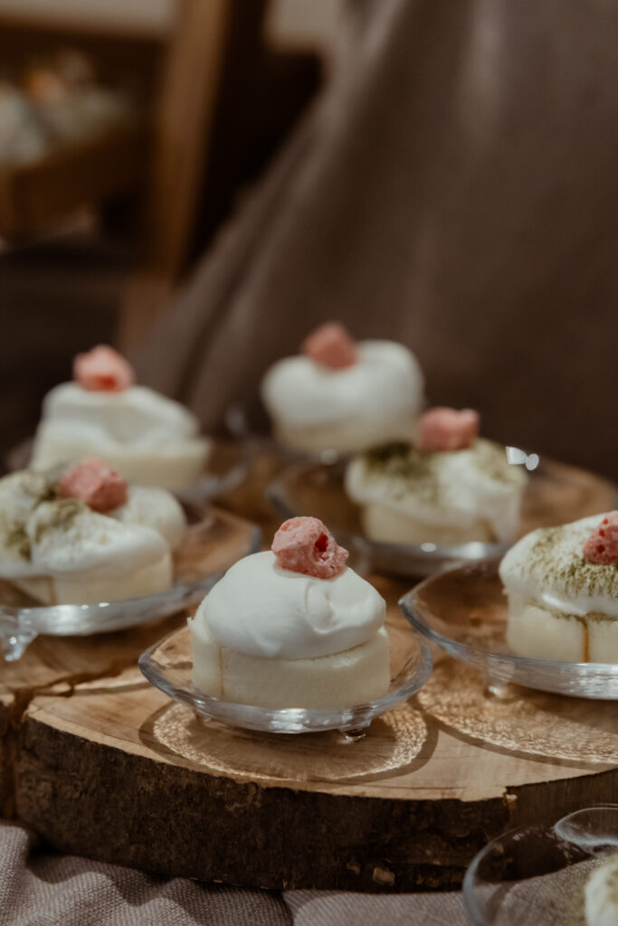 Small dessert portions with whipped cream and a pink garnish, served on transparent plates and arranged on a wooden board.