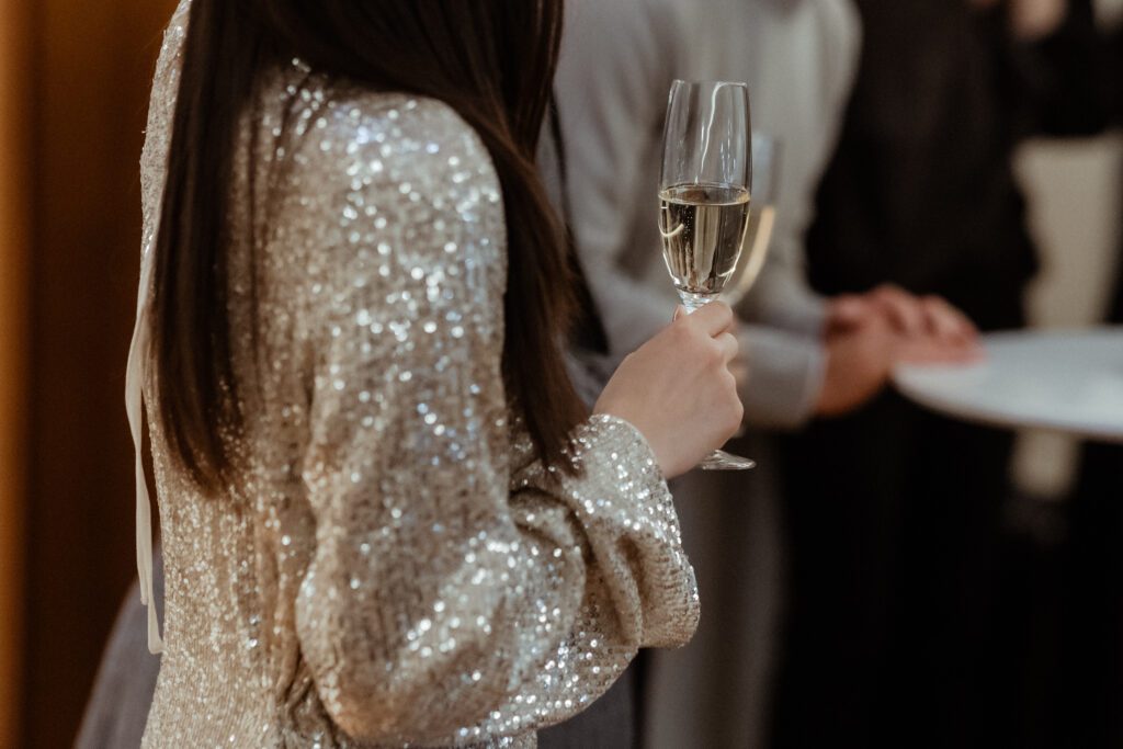 A person in a silver sequin dress holds a glass of champagne at a Korean wedding, adding an extra touch of elegance to the joyous social gathering.