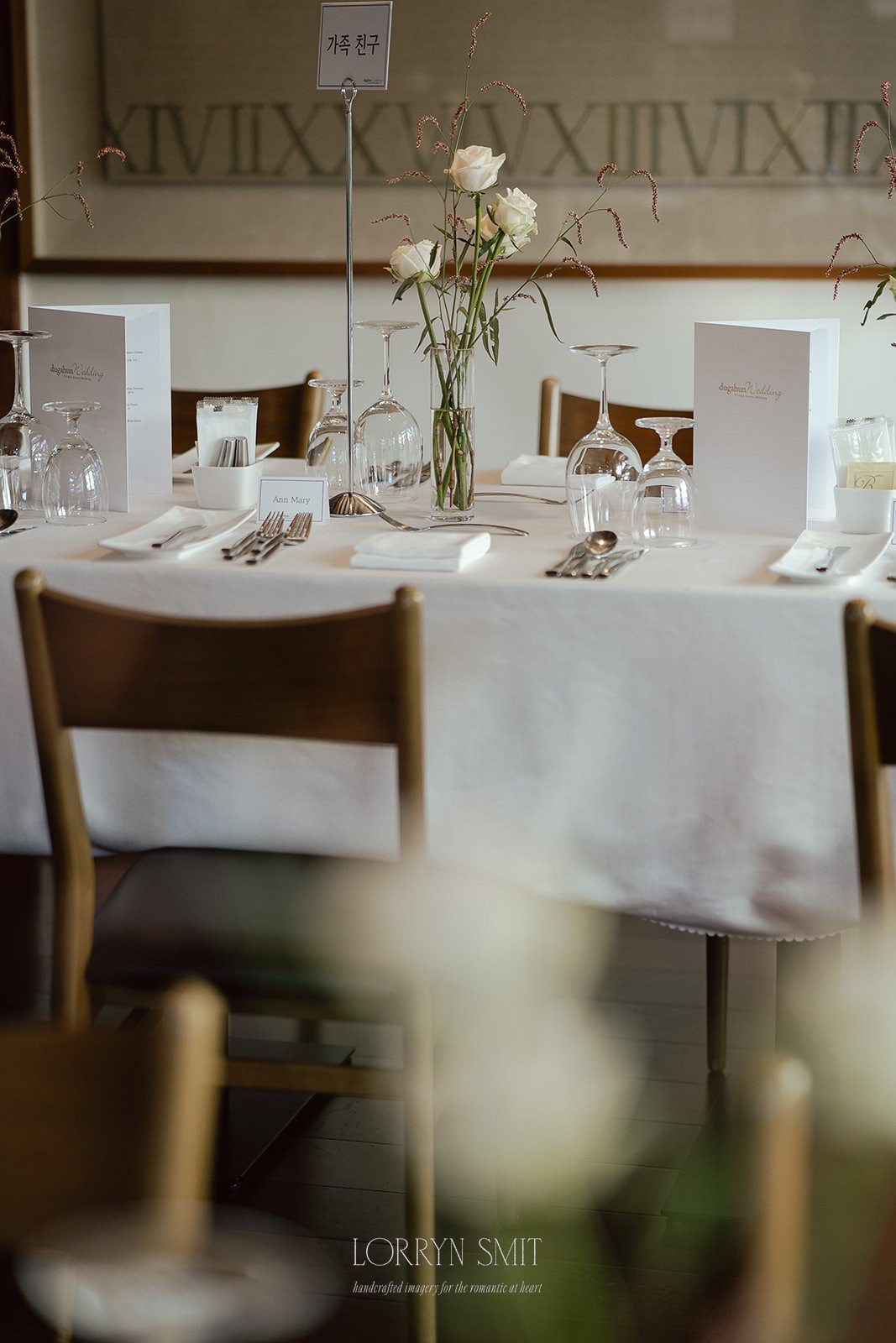 Round table set for a formal event with white tablecloth, glassware, menus, cutlery, and a floral centerpiece.