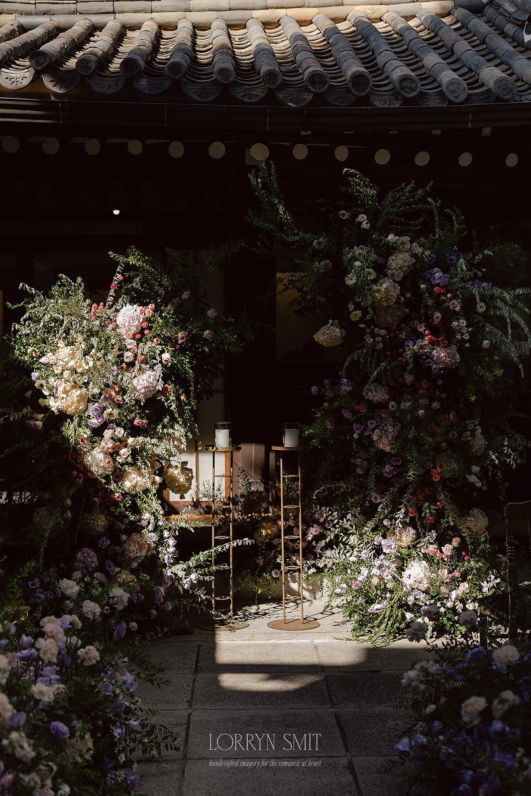 Flower arrangements and candles decorate the entrance of a building with a tiled roof, creating an elegant ceremonial ambiance—perfect for those seeking unique wedding venues in Korea.