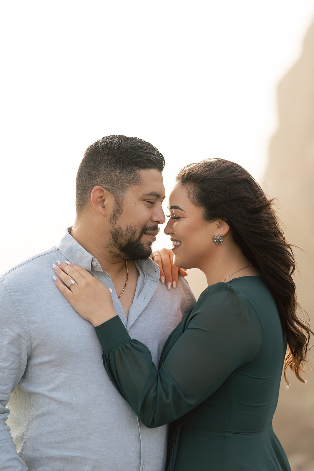 A couple stands close together outdoors, facing each other and smiling, taking pre-wedding photos before their Bali destination wedding. 