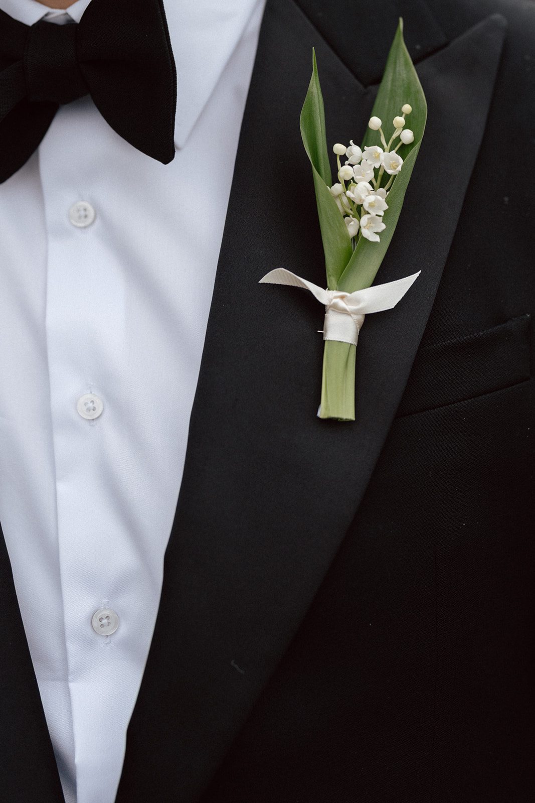 Close-up of a person in a black tuxedo, white shirt, and black bow tie, featuring a boutonniere with white flowers—perfect inspiration for couples choosing wedding venues in Korea.