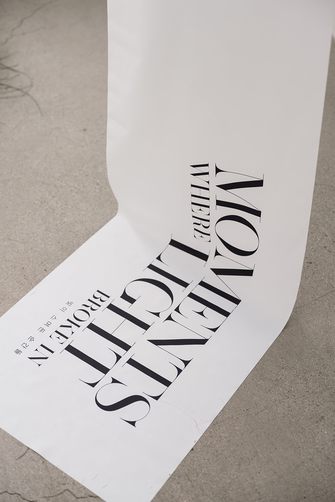 A large sheet of white paper with the bold black text "MOMENTS WHERE LIGHT BROKE IN" lies partially rolled out on a concrete floor.