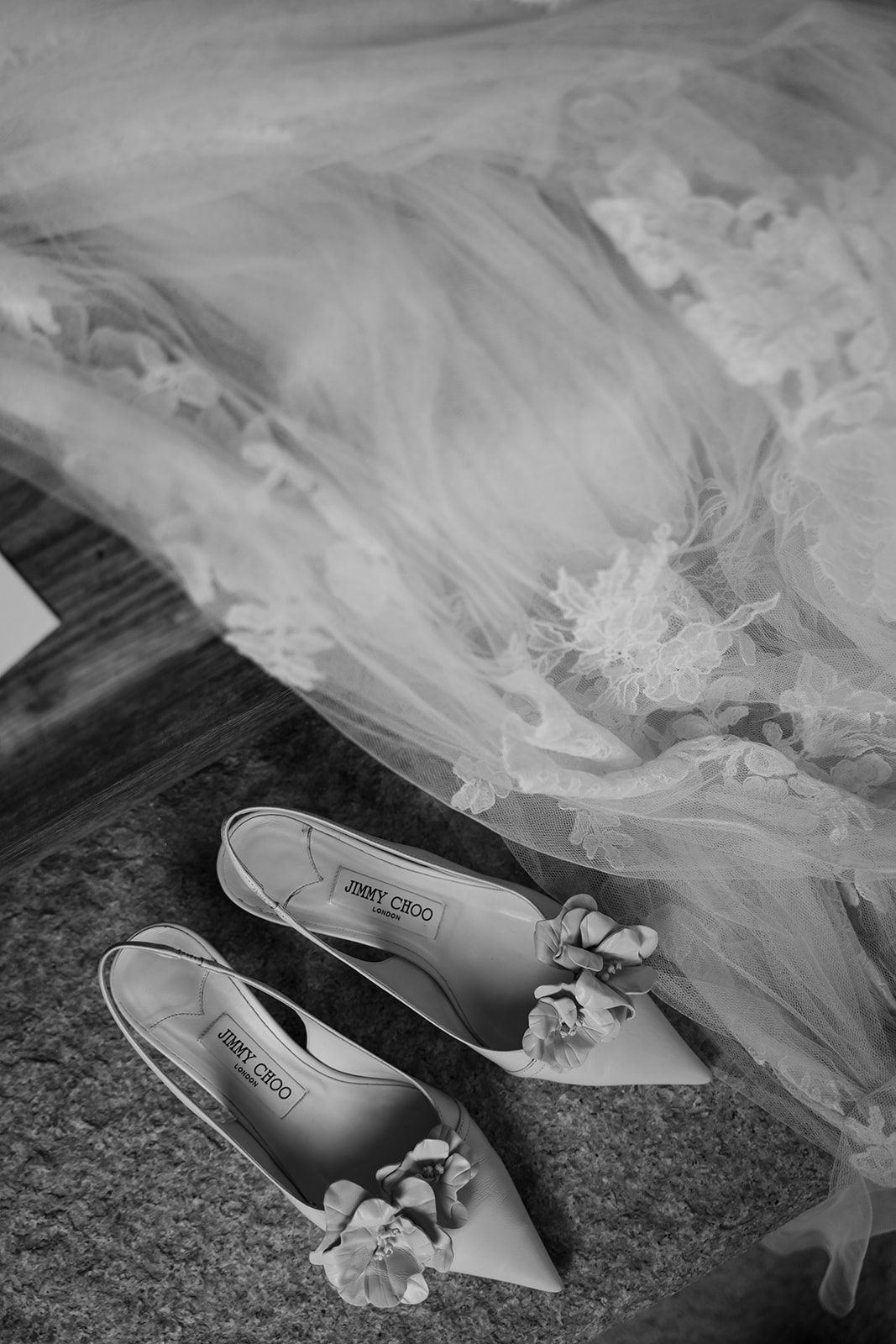 Black and white photo of Jimmy Choo floral-decorated heels beside a lace wedding dress spread out on the floor—a timeless moment for brides choosing wedding venues in Korea.