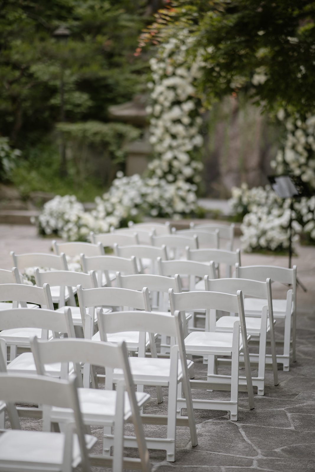 Rows of empty white folding chairs are arranged outdoors facing a floral arch, evoking the elegant charm often considered when choosing wedding venues in Korea for a picturesque garden ceremony.