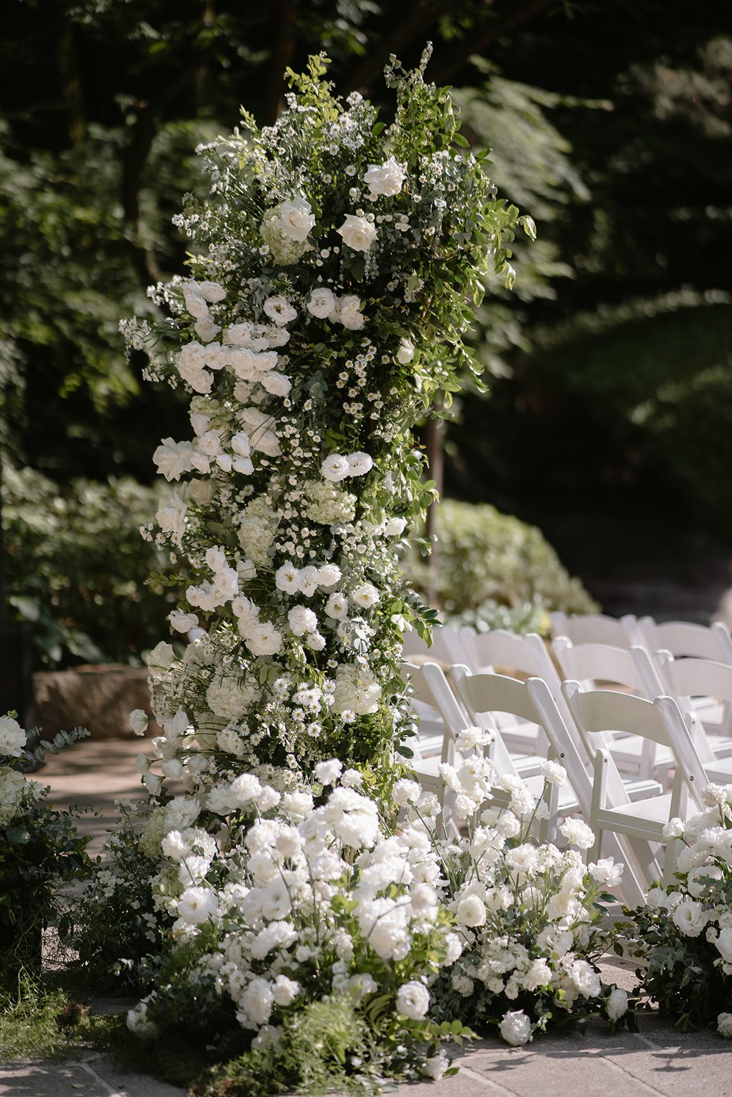 A vertical floral arrangement of white flowers and greenery stands beside rows of white folding chairs, offering inspiration for those choosing wedding venues in Korea’s beautiful outdoor settings.