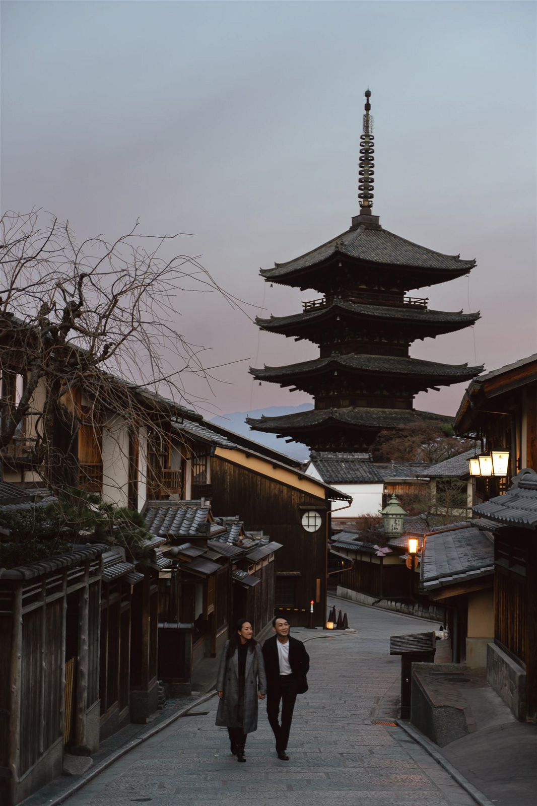 Two people walk down a quiet street lined with traditional wooden buildings, a multi-tiered pagoda glowing at dusk—a scene that captures the timeless charm of top Asia wedding destinations.